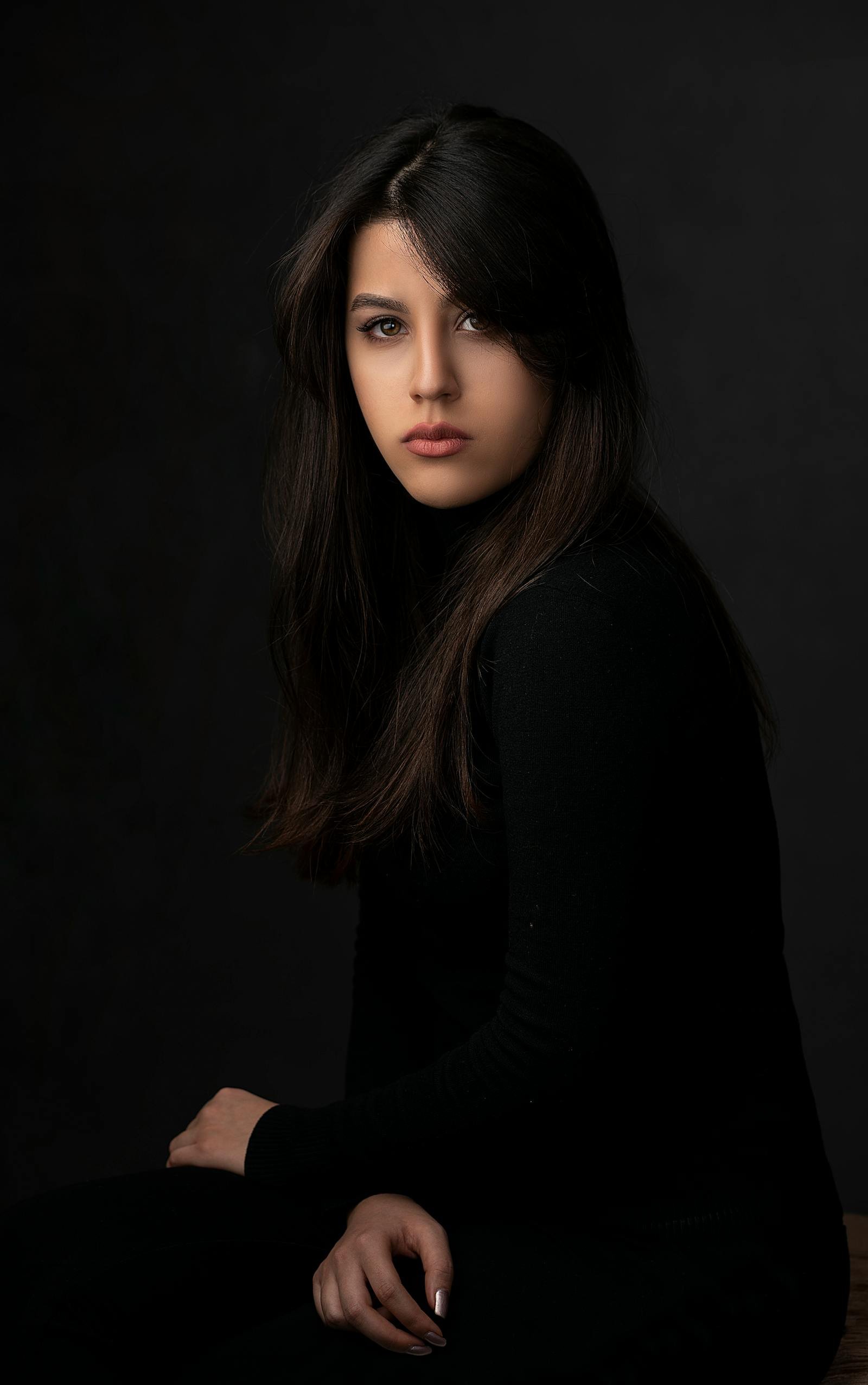 A studio portrait lit in warm tungsten — a young woman in profile against a deep charcoal seamless, soft fall-off on her shoulder, signature UONE Brand Studio lighting.