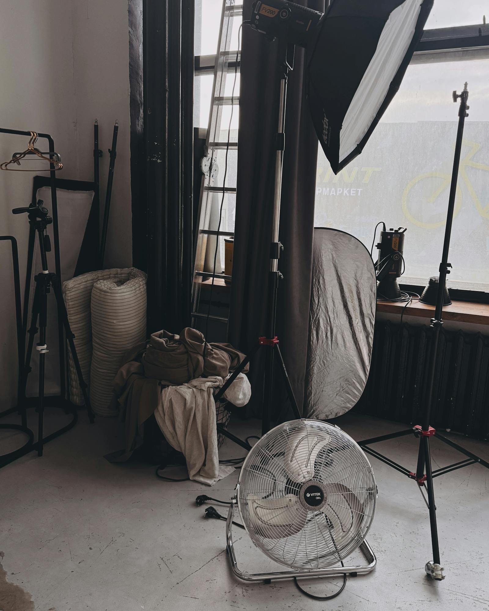 The Chennai studio with a tall north window, a rolled grey seamless, and two stylists steaming a garment on a rolling rack.